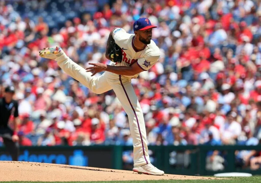 Philadelphia Phillies starter Cristopher Sánchez twists after delivering a pitch, with his left arm reaching back after the follow-through and his left leg extended behind him on a sunny day with the audience blurred behind him.